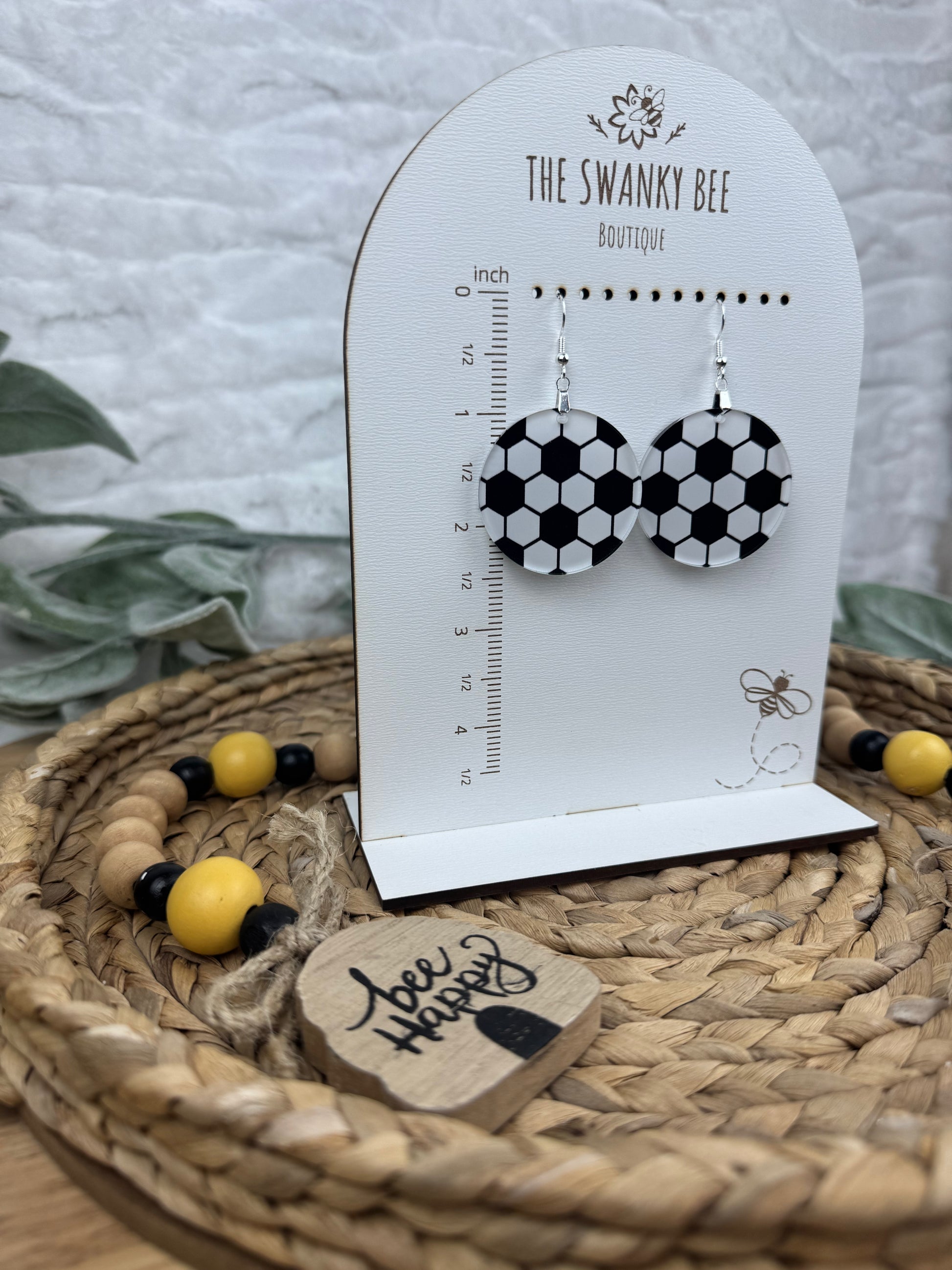 Stylish soccer earrings with black and white patterns, hanging on a branded card, displayed on a woven basket with decorative accents.