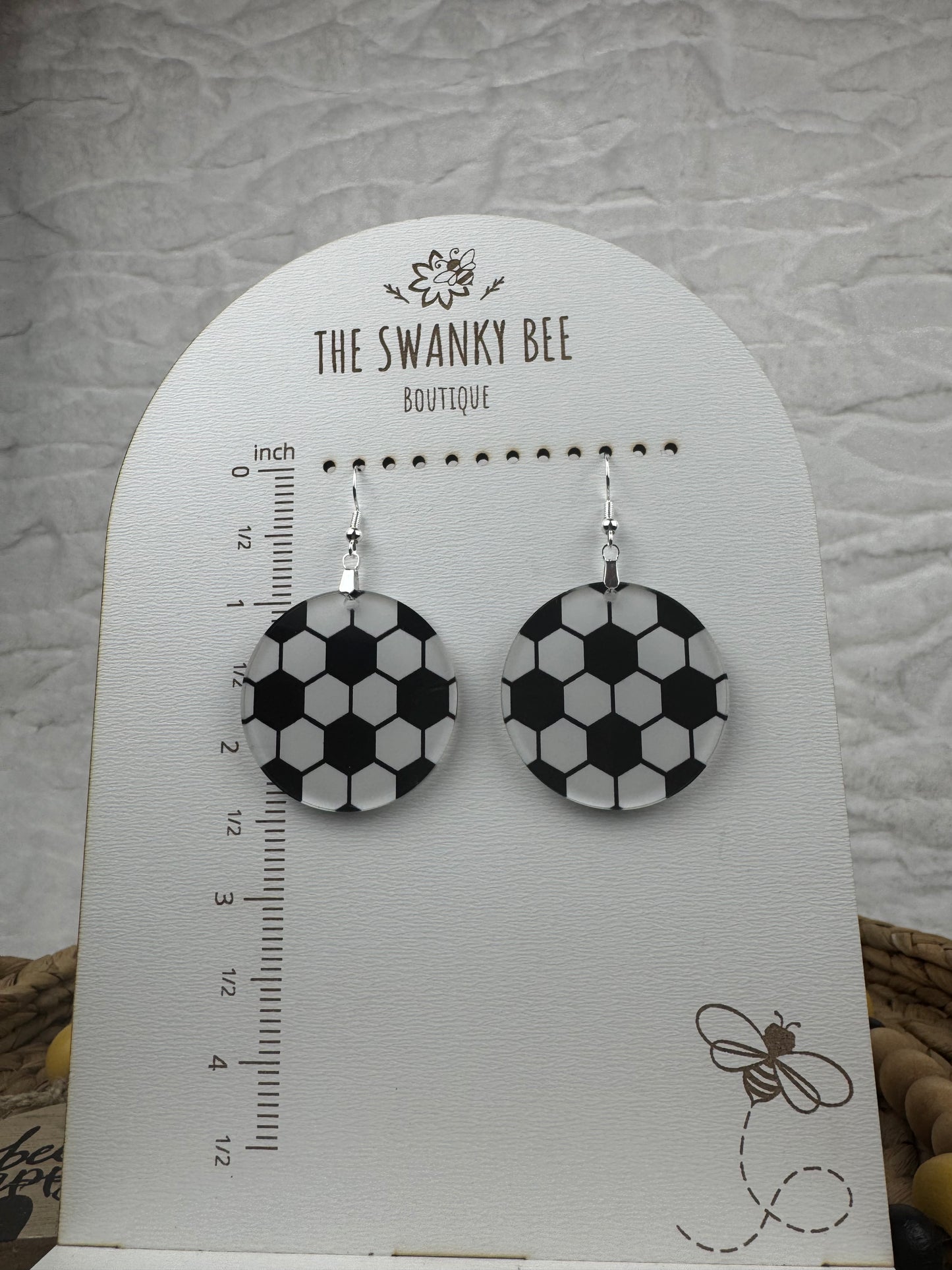 Soccer-themed earrings with black and white hexagonal patterns, hanging on a display card from The Swanky Bee Boutique, ideal for casual wear.