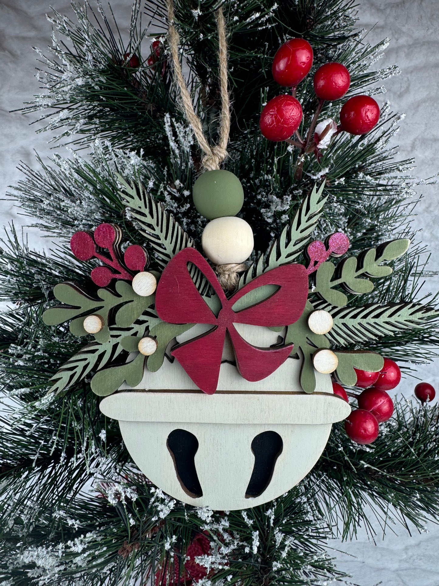 Handcrafted bell ornament with red bow and greenery on tree