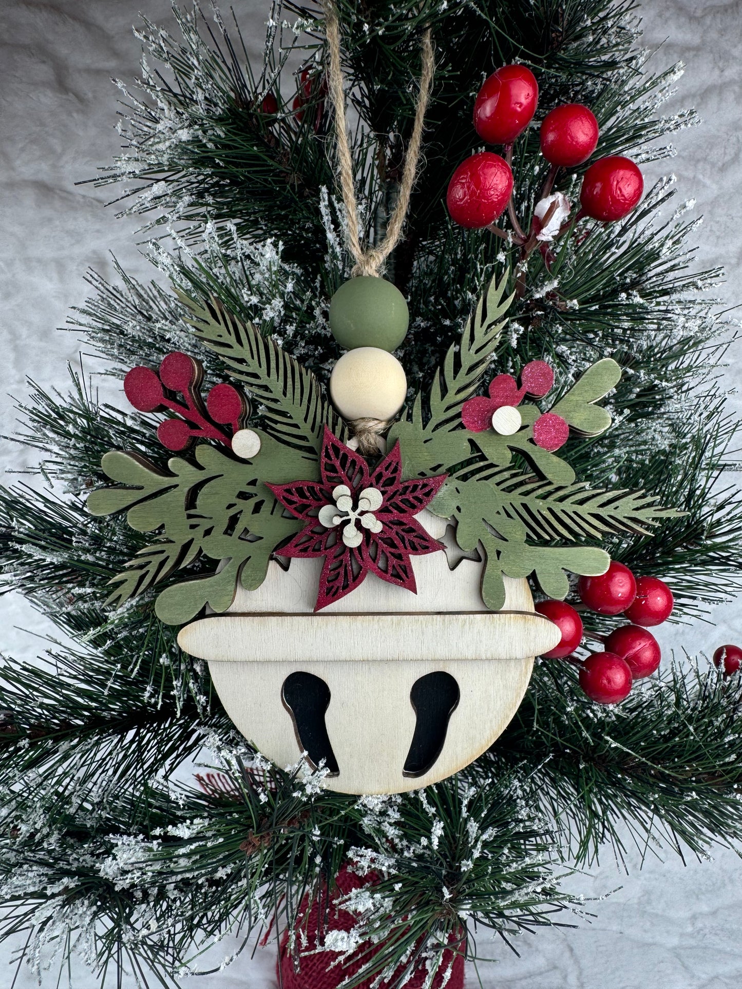 Handcrafted bell ornament with poinsettia and greenery on tree