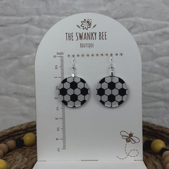 Lightweight soccer earrings with a black and white design, showcased on a branded card with a ruler guide, surrounded by decorative beads.