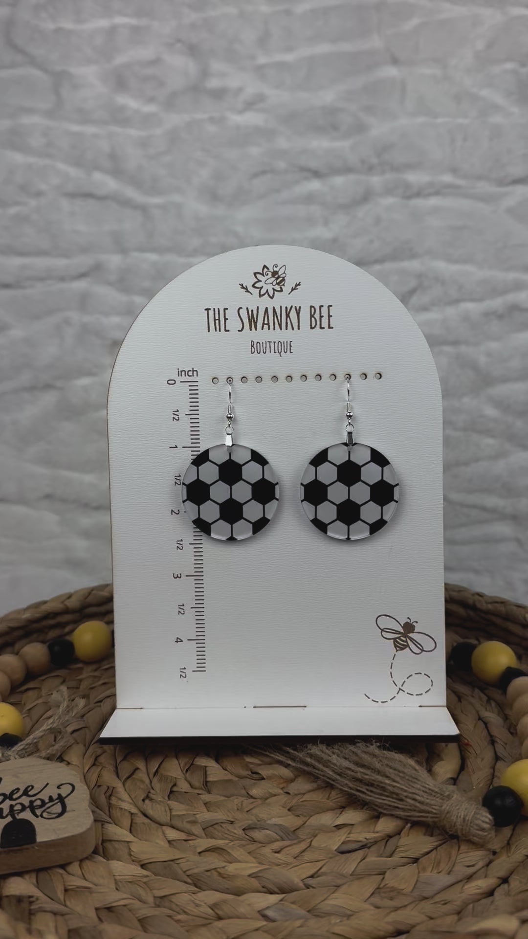 Lightweight soccer earrings with a black and white design, showcased on a branded card with a ruler guide, surrounded by decorative beads.