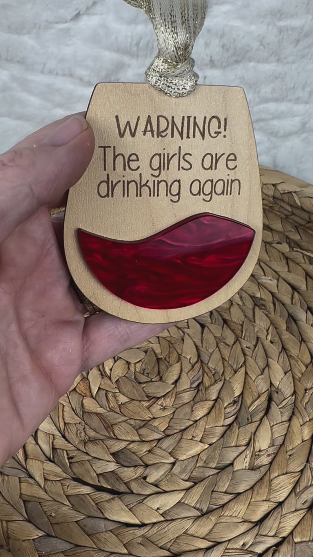 Hand holding ornament with 'Warning! The girls are drinking again'